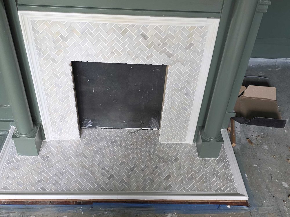 Fireplace surround with a marble herringbone hearth part way through installation
