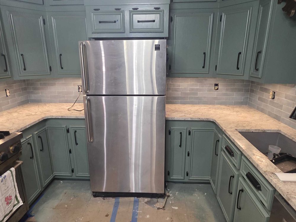 Green kitchen cabinets with stone counters and a tile backsplash