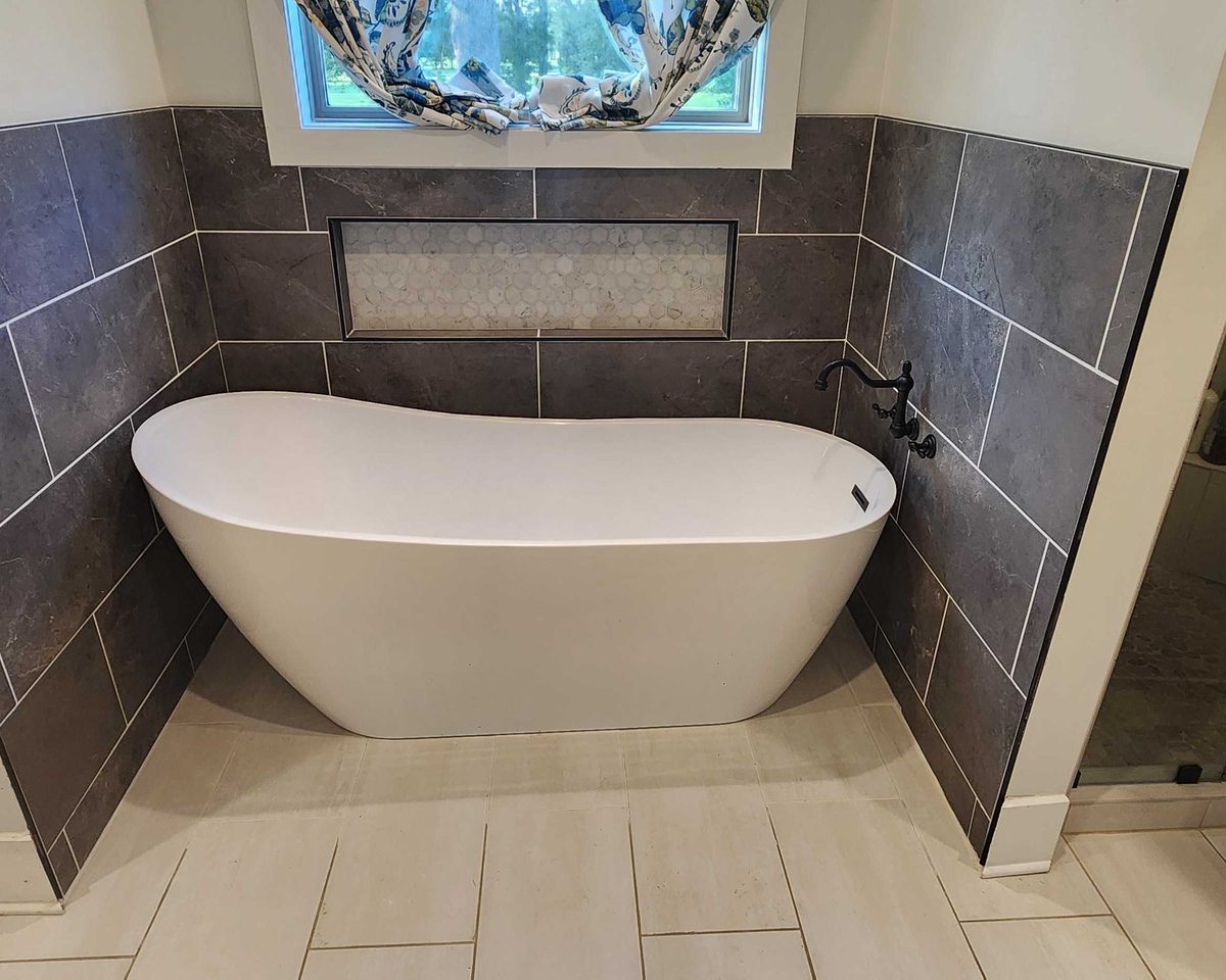 Freestanding soaking tub set into a slate tile surround beside a glass shower