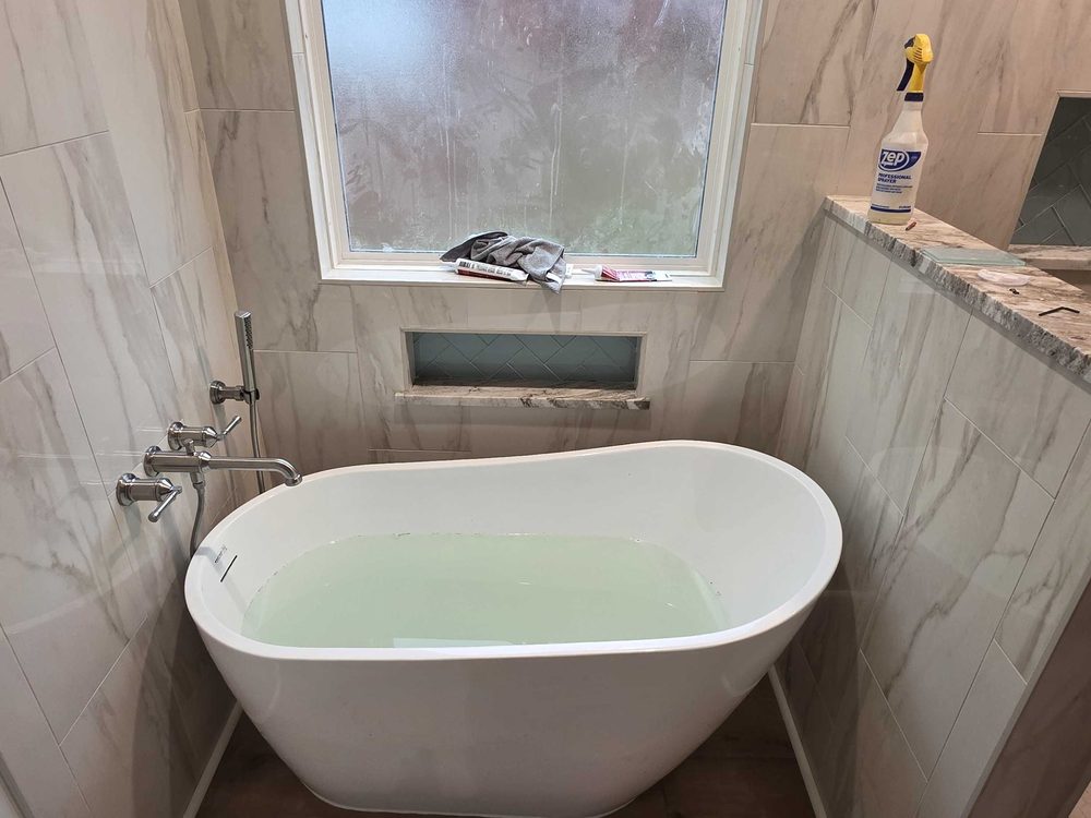 Finished bathroom with a freestanding tub against marble look tile