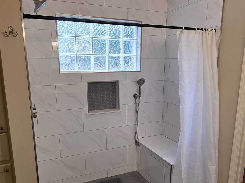 Tiled walk in shower with a bench, a recessed niche and a glass block window