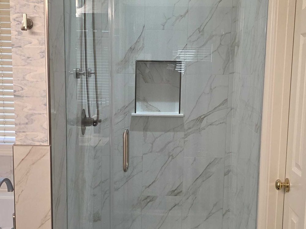 Frameless glass shower with marble look tile and a recessed niche