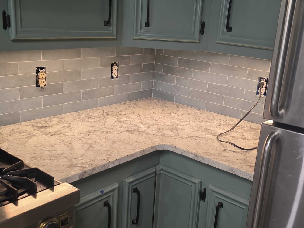 Green kitchen cabinets with a stone counter and tile backsplash