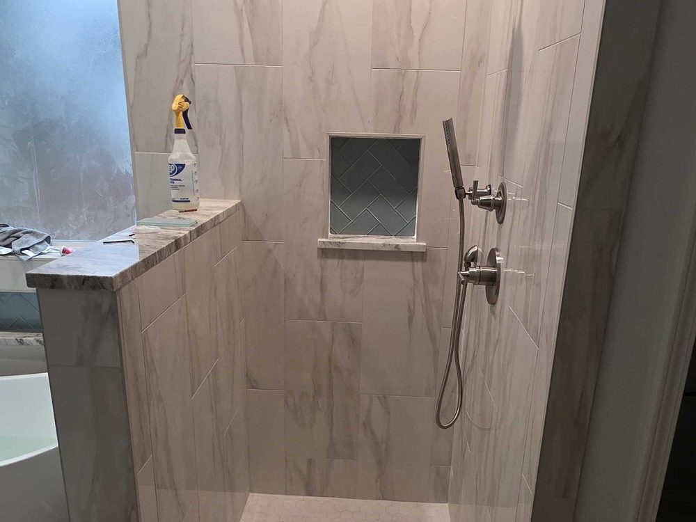 Walk in tile shower with a recessed niche and a tiled half wall