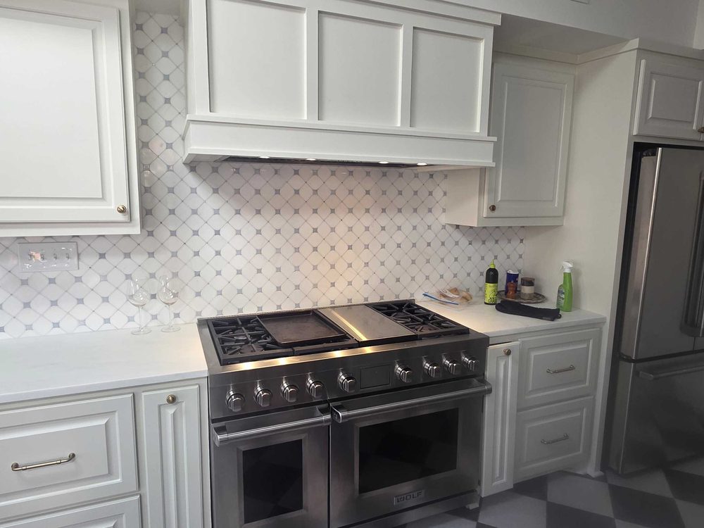 White kitchen cabinets and a range under a patterned tile backsplash